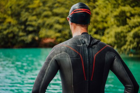 Foto de Athlete putting on a swimming suit and preparing for triathlon swimming and training in the river surrounded by natural greenery. - Imagen libre de derechos