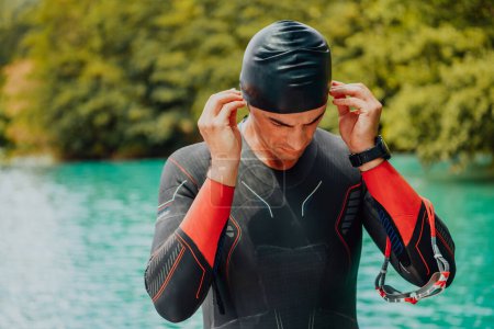 Photo for Athlete putting on a swimming suit and preparing for triathlon swimming and training in the river surrounded by natural greenery. - Royalty Free Image