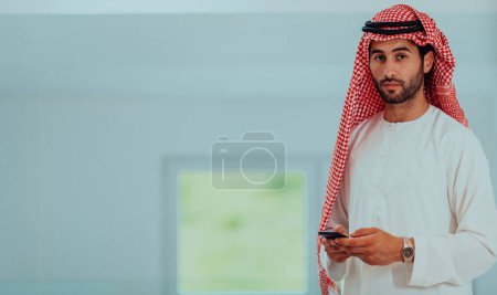 Foto de Young modern Muslim Arabian businessmen wearing traditional clothes while using smartphones at home - Imagen libre de derechos