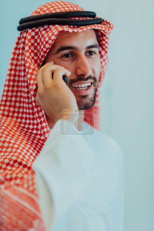 Téléchargez les photos : Young modern Muslim Arabian businessmen wearing traditional clothes while using smartphones at home - en image libre de droit