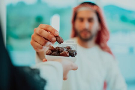 Photo for Modern multiethnic muslim family sharing a bowl of dates while enjoying iftar dinner together during a ramadan feast at home. - Royalty Free Image