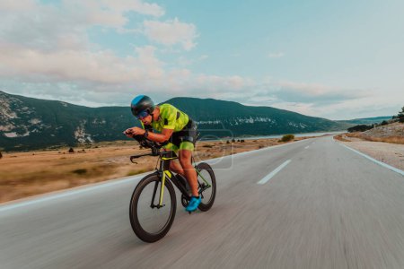 Foto de Full length portrait of an active triathlete in sportswear and with a protective helmet riding a bicycle. Selective focus. - Imagen libre de derechos