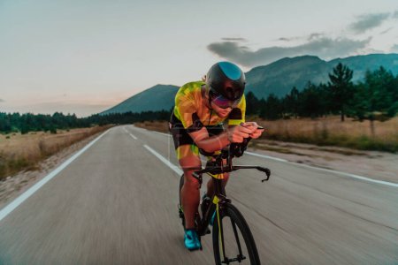 Photo for Night drive. Full length portrait of an active triathlete in sportswear and with a protective helmet riding a bicycle in night time.. Selective focus. - Royalty Free Image