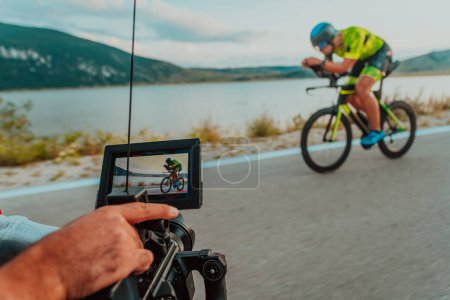 Photo for A cameraman with professional equipment and camera stabilization films a triathlete on the move riding a bicycle. - Royalty Free Image