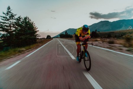 Téléchargez les photos : Night drive. Full length portrait of an active triathlete in sportswear and with a protective helmet riding a bicycle in night time.. Selective focus. - en image libre de droit
