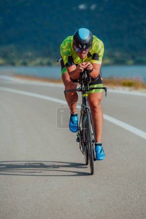 Photo for Full length portrait of an active triathlete in sportswear and with a protective helmet riding a bicycle. Selective focus. - Royalty Free Image