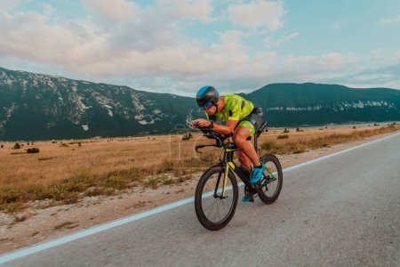 Photo for Full length portrait of an active triathlete in sportswear and with a protective helmet riding a bicycle. Selective focus. - Royalty Free Image