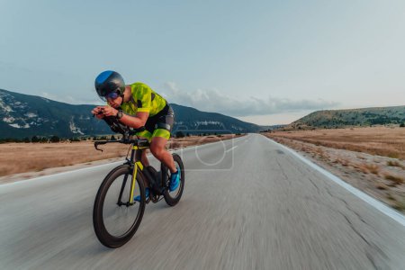 Foto de Full length portrait of an active triathlete in sportswear and with a protective helmet riding a bicycle. Selective focus. - Imagen libre de derechos