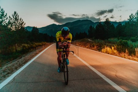 Foto de Conducción nocturna. Retrato completo de un triatleta activo en ropa deportiva y con un casco protector montando una bicicleta en la noche. Enfoque selectivo. - Imagen libre de derechos