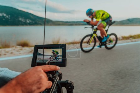 Foto de A cameraman with professional equipment and camera stabilization films a triathlete on the move riding a bicycle. - Imagen libre de derechos