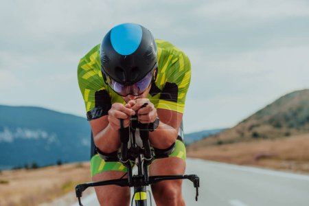 Téléchargez les photos : Close up photo of an active triathlete in sportswear and with a protective helmet riding a bicycle. Selective focus. - en image libre de droit