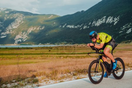 Téléchargez les photos : Full length portrait of an active triathlete in sportswear and with a protective helmet riding a bicycle. Selective focus. - en image libre de droit