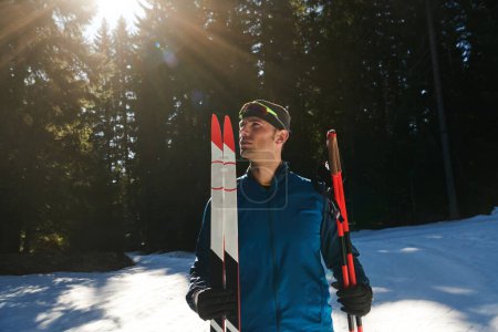 Foto de Retrato apuesto atleta masculino con esquís de fondo en las manos y gafas, entrenamiento en el bosque nevado. Concepto de estilo de vida saludable invierno - Imagen libre de derechos