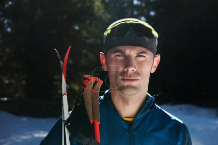 Photo for Portrait handsome male athlete with cross country skis in hands and goggles, training in snowy forest. Healthy winter lifestyle concept - Royalty Free Image