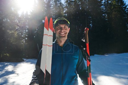 Foto de Portrait handsome male athlete with cross country skis in hands and goggles, training in snowy forest. Healthy winter lifestyle concept - Imagen libre de derechos