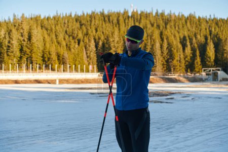 Téléchargez les photos : Handsome male athlete with cross country skis, taking fresh breath and having break after hard workout training in a snowy forest. Checking smartwatch. Healthy winter lifestyle. - en image libre de droit