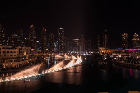 Téléchargez les photos : Dubai singing fountains at night lake view between skyscrapers. City skyline in dusk modern architecture in UAE capital downtown. High quality 4k footage - en image libre de droit