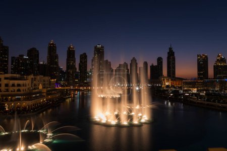 Téléchargez les photos : Dubaï chantant fontaines à la nuit vue sur le lac entre les gratte-ciel. Skyline de la ville au crépuscule architecture moderne dans la capitale des Émirats arabes unis centre-ville. Images 4k de haute qualité - en image libre de droit