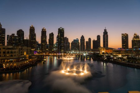 Foto de Dubai singing fountains at night lake view between skyscrapers. City skyline in dusk modern architecture in UAE capital downtown. High quality 4k footage - Imagen libre de derechos