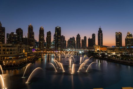 Téléchargez les photos : Dubai singing fountains at night lake view between skyscrapers. City skyline in dusk modern architecture in UAE capital downtown. High quality 4k footage - en image libre de droit