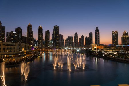 Foto de Dubai singing fountains at night lake view between skyscrapers. City skyline in dusk modern architecture in UAE capital downtown. High quality 4k footage - Imagen libre de derechos