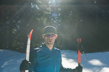Photo for Portrait handsome male athlete with cross country skis in hands and goggles, training in snowy forest. Healthy winter lifestyle concept - Royalty Free Image