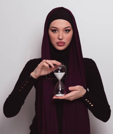 Téléchargez les photos : Belle femme d'affaires arabe portant hijab et tenant horloge de sable. Le temps passe et c'est un concept de pression. Photo de haute qualité - en image libre de droit