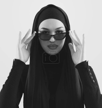 Foto de Retrato de una hermosa mujer musulmana joven y elegante que usa hijab negro y gafas de sol como concepto moderno de moda oriental posando sobre fondo blanco. Foto de alta calidad - Imagen libre de derechos