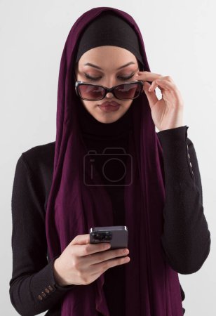 Téléchargez les photos : Femme en noir élégant vêtements à la mode foulard musulman. Dame utilisant un téléphone intelligent, portrait rapproché d'une fille souriante du Moyen-Orient. Photo de haute qualité - en image libre de droit
