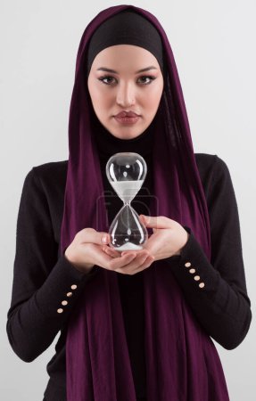 Foto de Hermosa mujer de negocios árabe vistiendo hijab y sosteniendo reloj de arena. El tiempo pasa y es un concepto de presión. Foto de alta calidad - Imagen libre de derechos