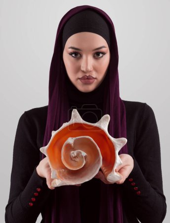 Foto de Mujer musulmana bastante elegante usando hijab y sosteniendo una concha marina y sueños cerrados ojos. Relación dorada y concepto de proporción ideal.Foto de alta calidad - Imagen libre de derechos