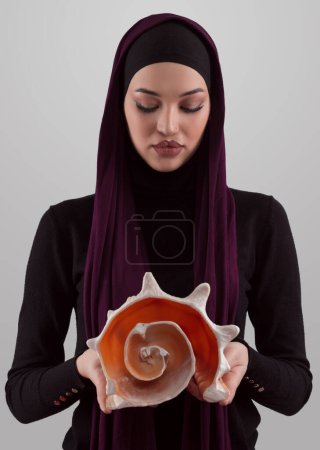 Photo for Pretty stylish Muslim woman wearing hijab and holding a seashell and dreams closed eyes. Golden ratio and ideal proportion concept.High quality photo - Royalty Free Image