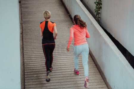 Foto de Two women in sports clothes running in a modern urban environment. The concept of a sporty and healthy lifestyle. - Imagen libre de derechos