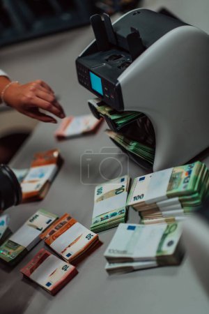 Photo for Bank employees using money counting machine while sorting and counting paper banknotes inside bank vault. Large amounts of money in the bank. - Royalty Free Image