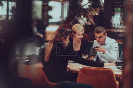 Téléchargez les photos : Photo through the glass of a group of business people sitting in a cafe and discussing business plans and ideas for new online commercial services. - en image libre de droit