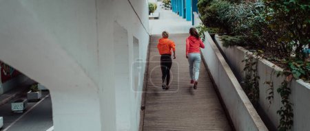 Téléchargez les photos : Two women in sports clothes running in a modern urban environment. The concept of a sporty and healthy lifestyle. - en image libre de droit