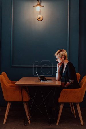 Téléchargez les photos : Businesswoman sitting in a cafe while focused on working on a laptop and participating in an online meetings. Selective focus - en image libre de droit