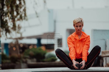 Foto de Fit attractive woman in sportswear stretching one leg before jogging on the footpath outdoor in summer among greenery. Workout, sport, activity, fitness, vacation and training conept - Imagen libre de derechos