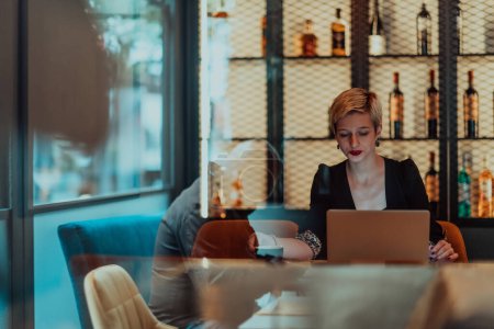 Téléchargez les photos : Femme d'affaires assis dans un café tout en se concentrant sur le travail sur un ordinateur portable et de participer à des réunions en ligne. Concentration sélective - en image libre de droit