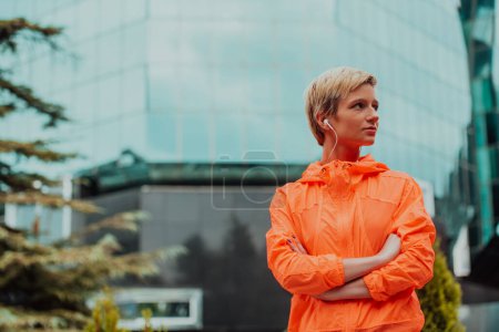Photo for A woman in a sports outfit is resting in a city environment after a hard morning workout while using noiseless headphones. - Royalty Free Image