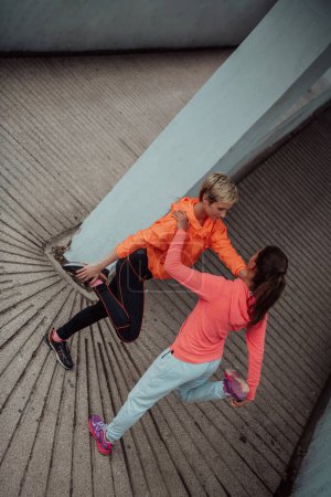Foto de Two women warming up together and preparing for a morning run in an urban environment. Selective focus . - Imagen libre de derechos