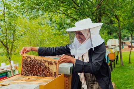 Foto de Hijab Arabian woman checking the quality of honey on the large bee farm in which she invested. - Imagen libre de derechos