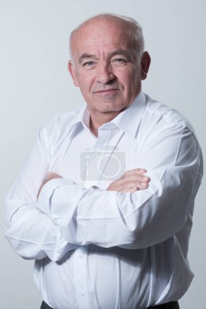 Photo for Confident senior man in white shirt crossing hands on chest and looking at camera while standing against gray background. Self confident senior isolated white studio shoot. High quality photo - Royalty Free Image