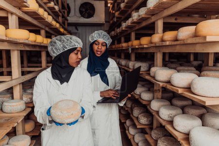 Foto de Business of a Muslim partners in a cheese warehouse, checking the quality of cheese and entering data into laptop. - Imagen libre de derechos