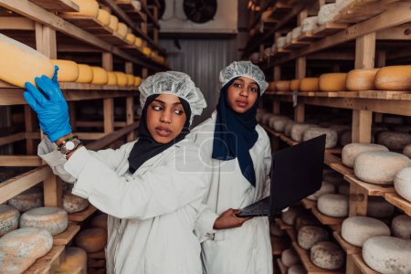 Téléchargez les photos : Business of a Muslim partners in a cheese warehouse, checking the quality of cheese and entering data into laptop. - en image libre de droit