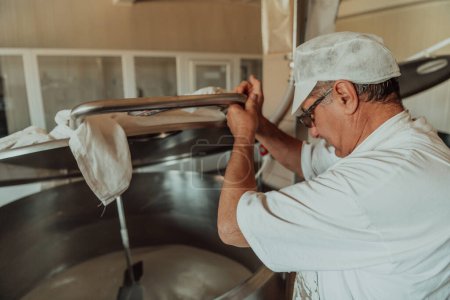 Téléchargez les photos : Homme mélangeant le lait dans le réservoir en acier inoxydable pendant le processus de fermentation lors de la fabrication du fromage
. - en image libre de droit