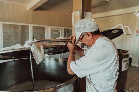 Hombre mezclando leche en el tanque de acero inoxidable durante el proceso de fermentación en la fabricación de queso
. 