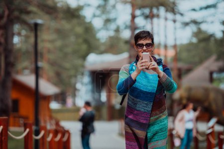 Téléchargez les photos : A woman in a fashionable outfit using a smartphone while spending time in the park on a beautiful sunny day. - en image libre de droit