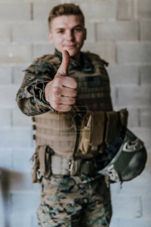 Photo for The soldier makes a gesture of success with his hand. A soldier in full war gear stands in front of a stone wall and shows the ok sign with his finger. - Royalty Free Image
