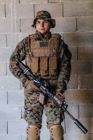 Foto de Un soldado de uniforme se para frente a una pared de piedra con todo el equipo de guerra preparándose para la batalla. - Imagen libre de derechos